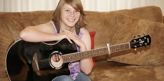 Young girl holding an acoustic guitar while sitting on a couch