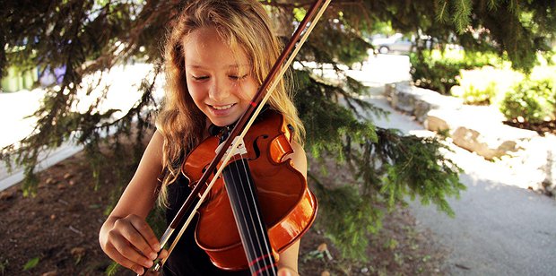 Girl playing violin outdoors at a summer music camp, building confidence and musical skills