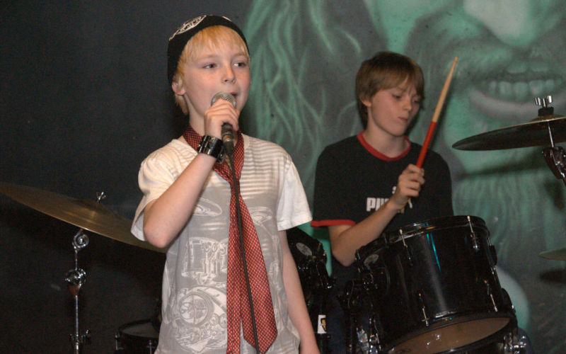 Child singing into a microphone while performing with a drummer